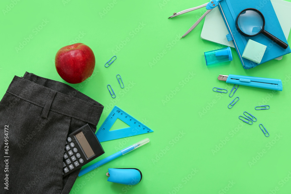 School pants with calculator fresh red apple and different stationery on green background