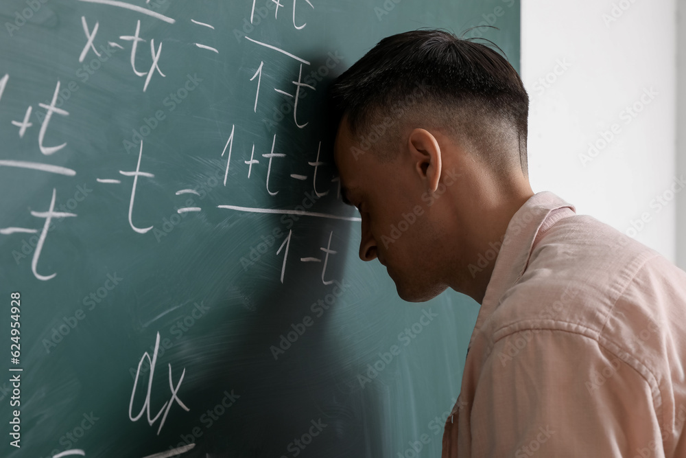 Tired Math teacher near chalkboard in classroom