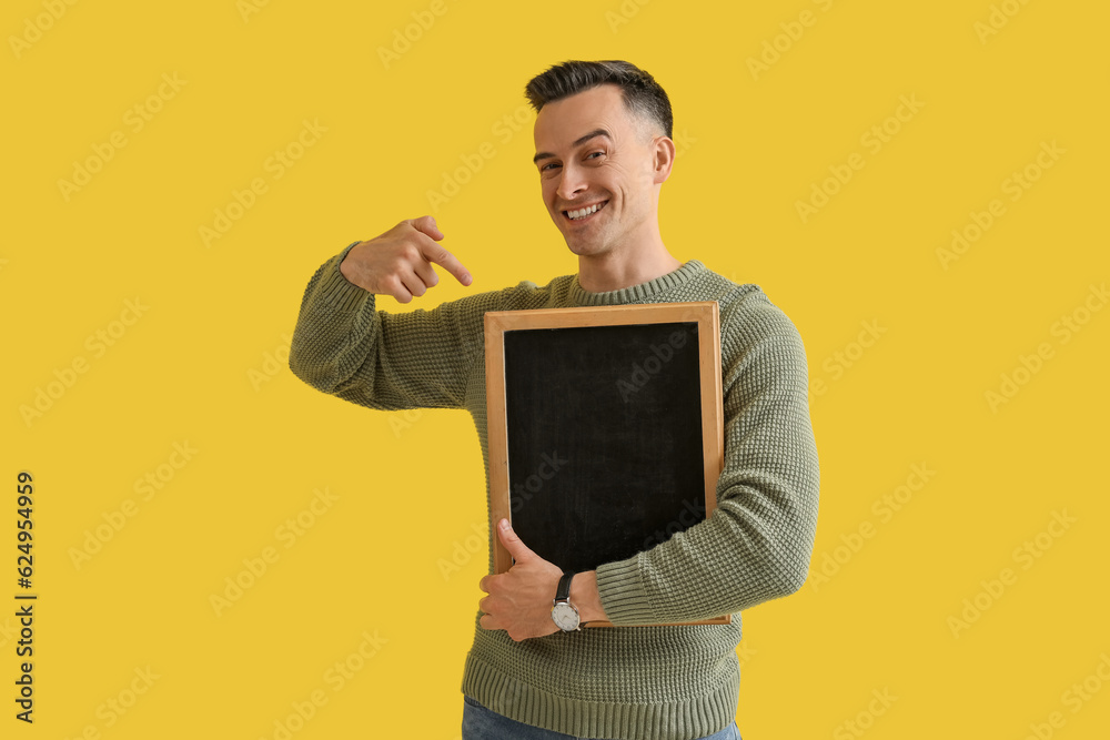 Male teacher pointing at chalkboard on yellow background