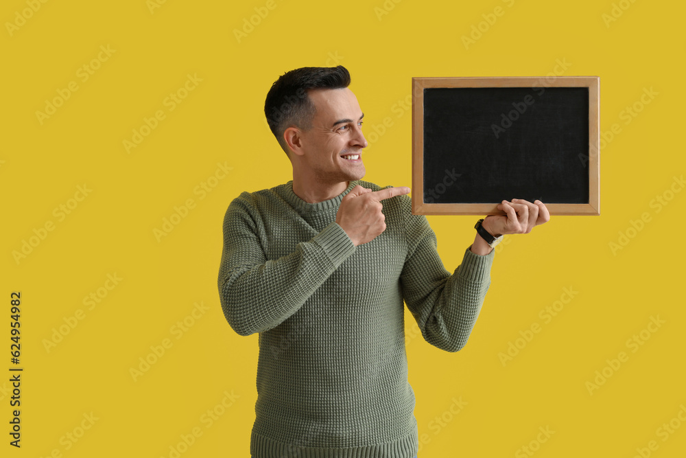 Male teacher pointing at chalkboard on yellow background