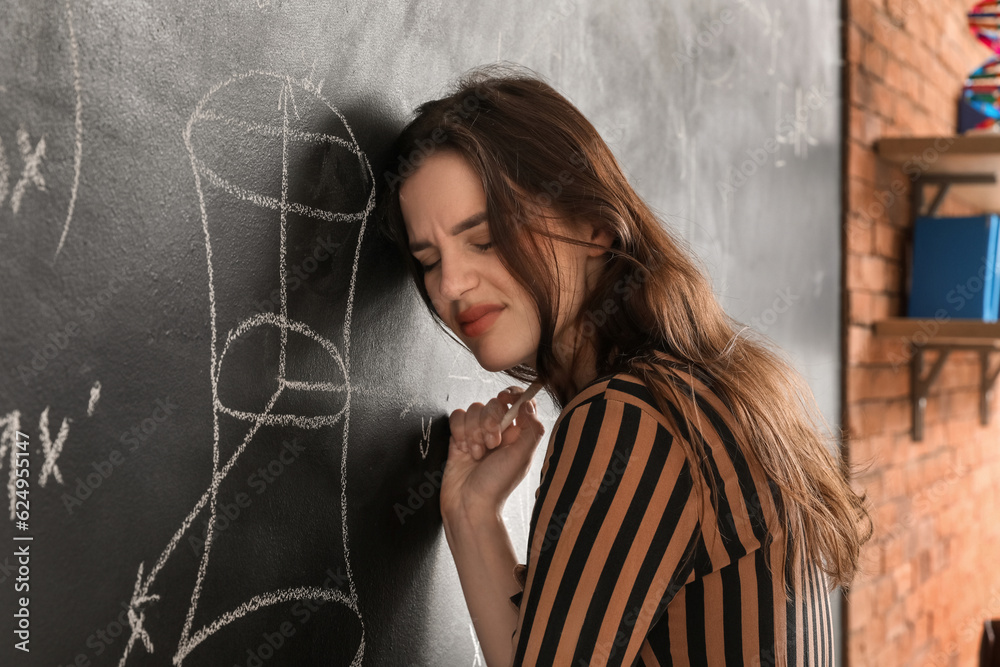 Stressed female Math teacher near blackboard in classroom