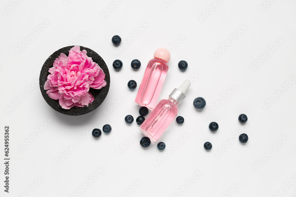 Composition with bottles of cosmetic products, blueberry and peony flower on white background