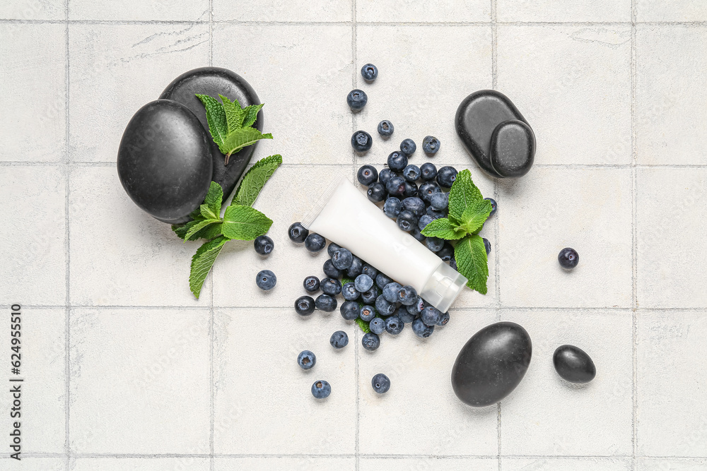 Composition with cosmetic product, spa stones, blueberry and mint leaves on light tile background