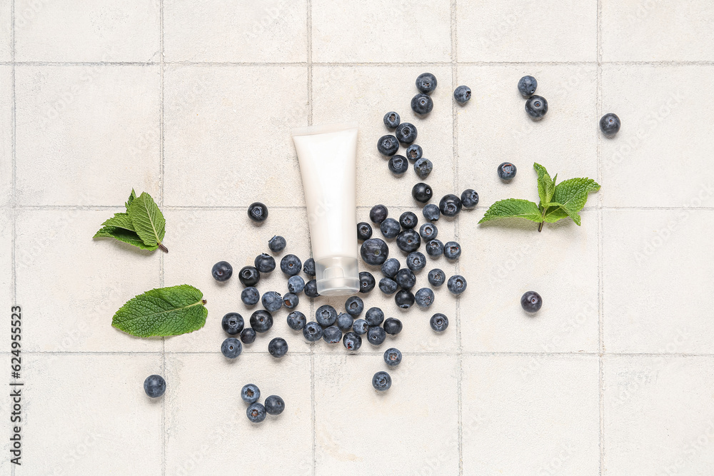 Composition with cosmetic product, mint leaves and blueberry on light tile background