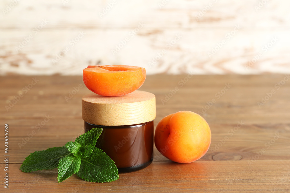 Jar with cosmetic cream and apricots on wooden table