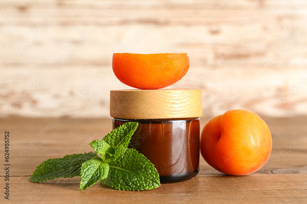 Jar with cosmetic cream and apricots on wooden table