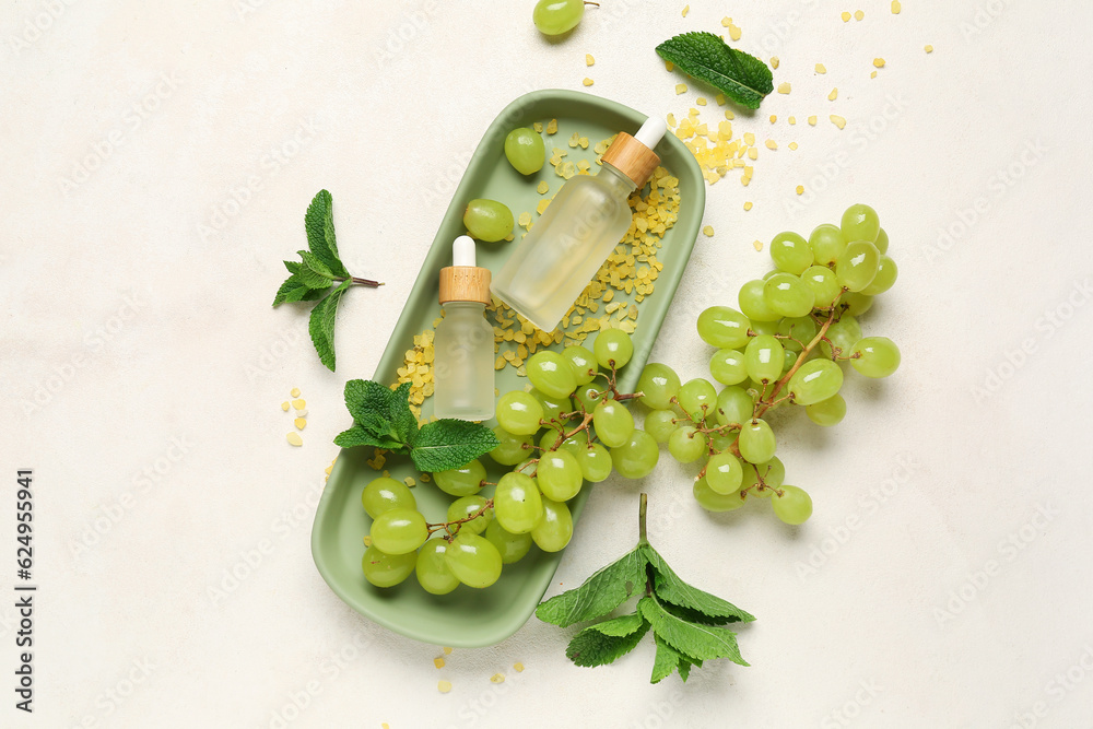 Bottles with cosmetic oil, sea salt and grapes on white background