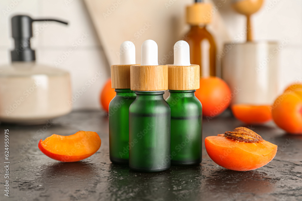 Bottles with cosmetic oil and apricots on black table