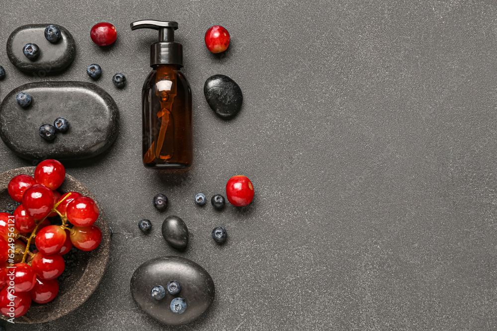 Bottle with cosmetic oil, grapes and blueberries on black background