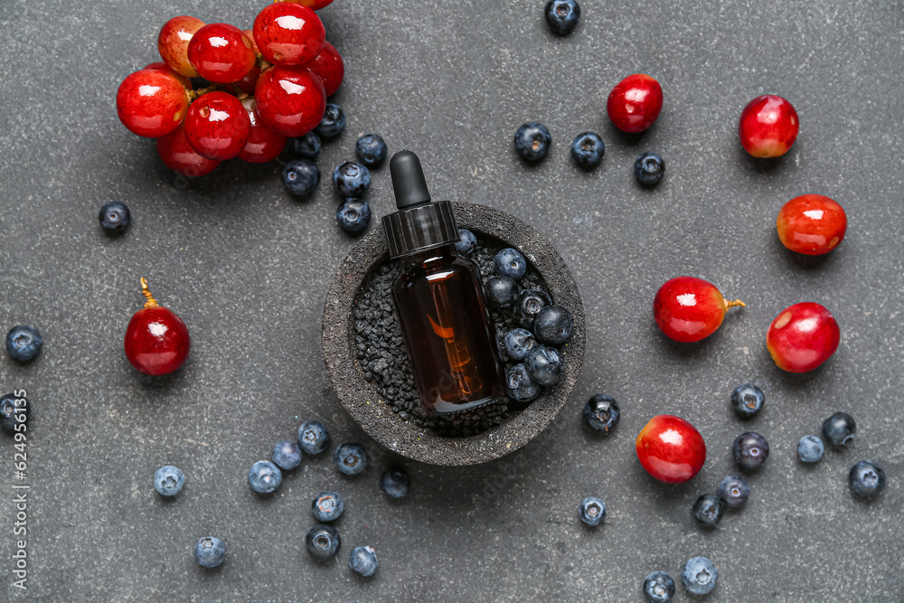 Bottle with cosmetic oil, sea salt, grapes and blueberries on black background