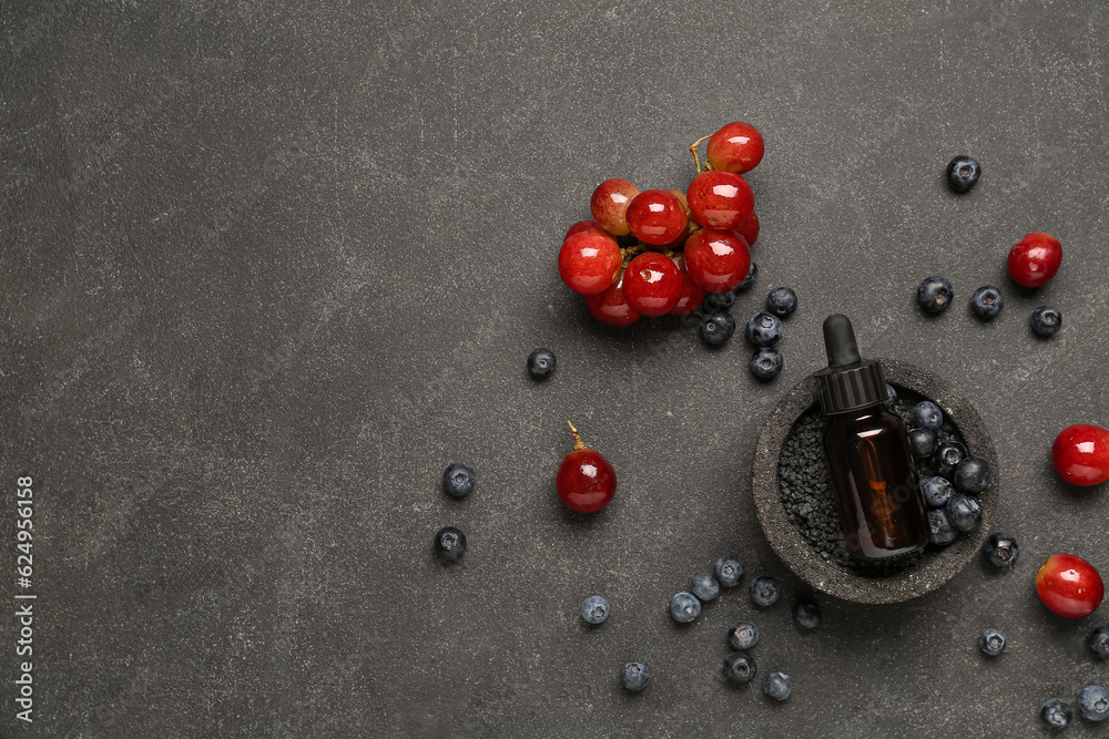 Bottle with cosmetic oil, sea salt, grapes and blueberries on black background