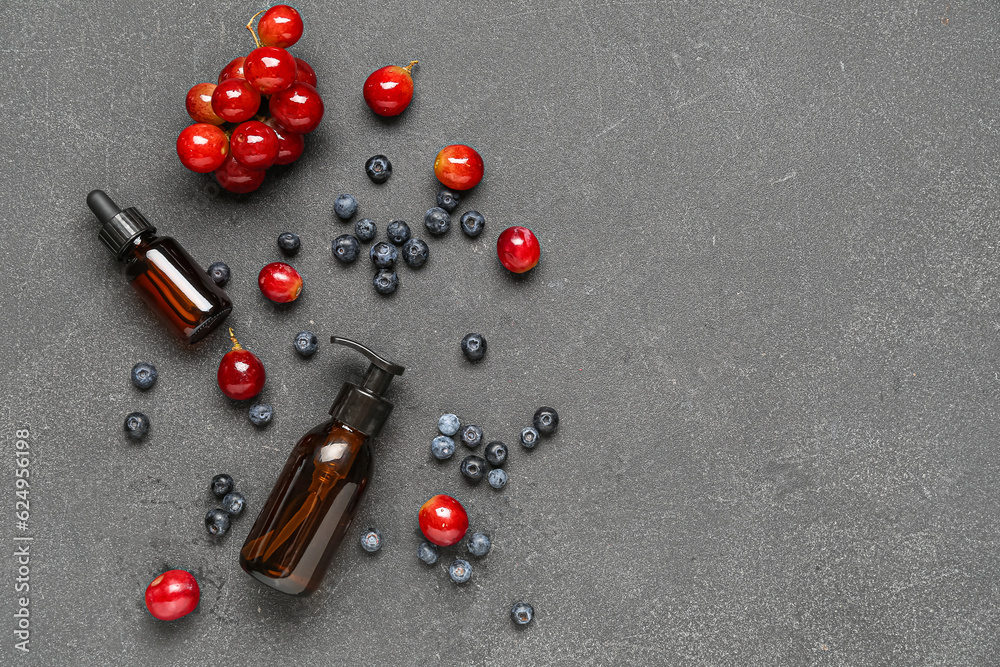 Bottles with cosmetic oil, grapes and blueberries on black background