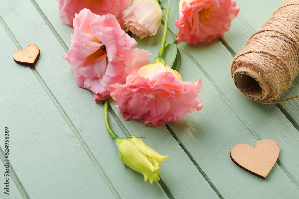 Beautiful pink eustoma flowers and threads on green wooden background