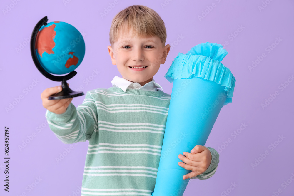 Happy little boy with blue school cone and globe on lilac background