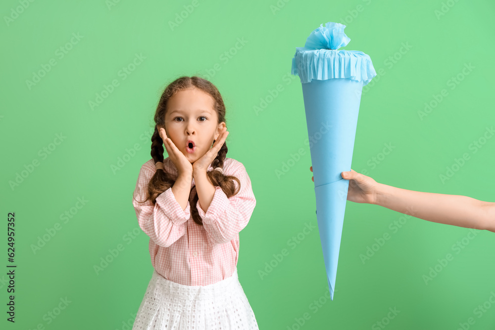 Mother greeting her happy little daughter with blue school cone on green background