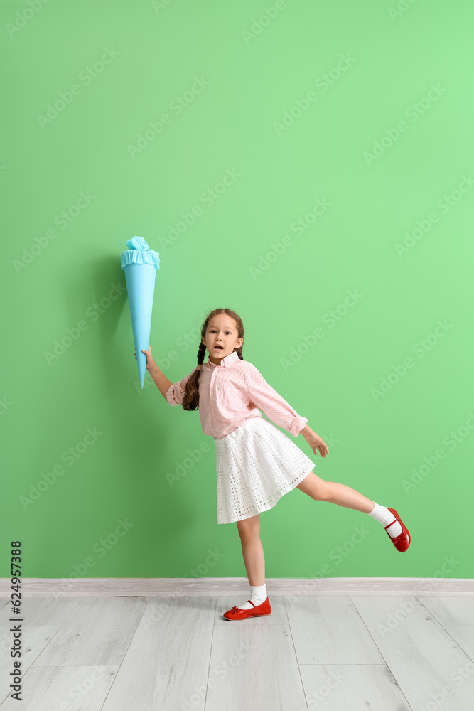 Little girl with blue school cone near green wall