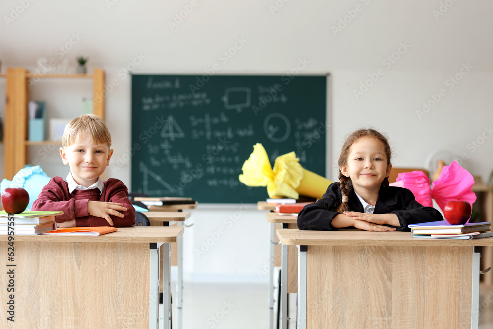 Happy classmates with school cones sitting at desks in classroom