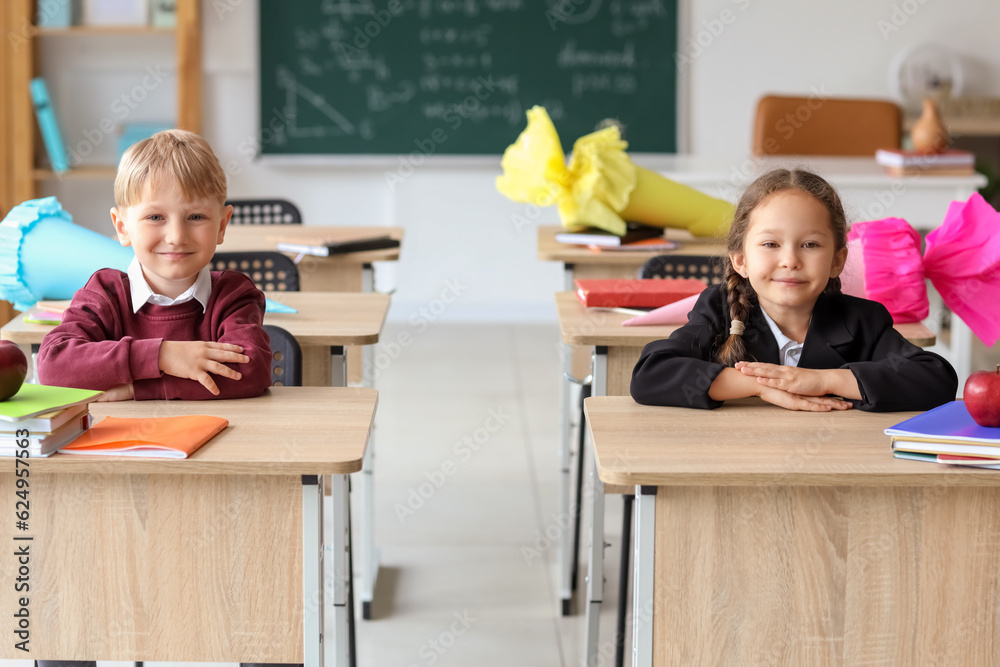 Happy classmates with school cones sitting at desks in classroom