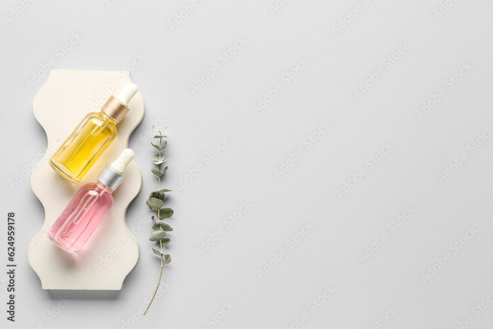 Plaster podium with bottles of essential oil and eucalyptus branch on light background