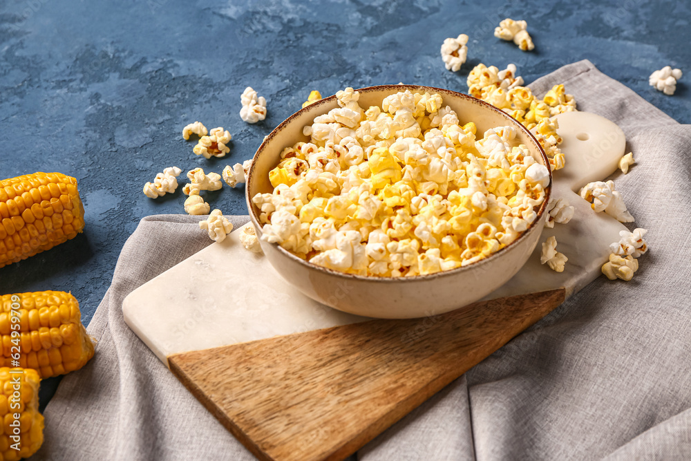 Bowl with tasty popcorn on blue background