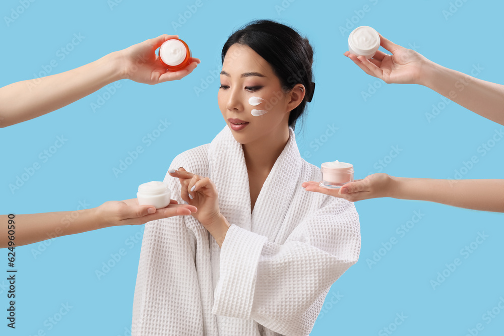 Beautiful Asian woman and hands with different creams on blue background