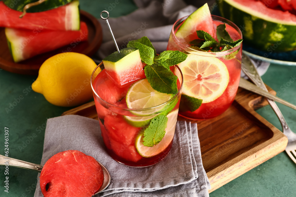 Wooden board with glasses of fresh watermelon lemonade and mint on green table