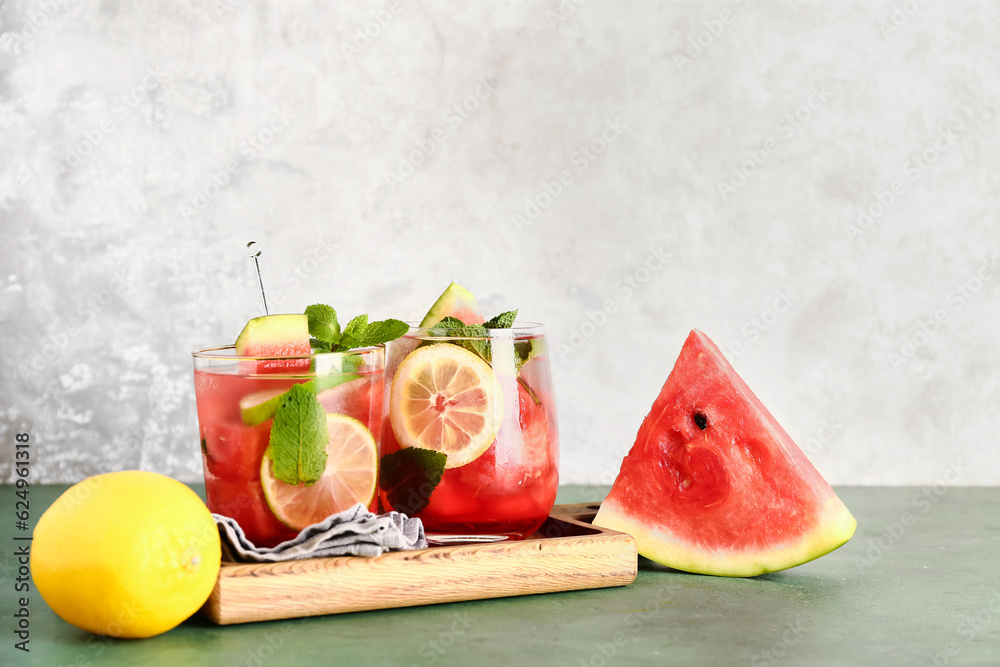 Wooden board with glasses of fresh watermelon lemonade and mint on green table