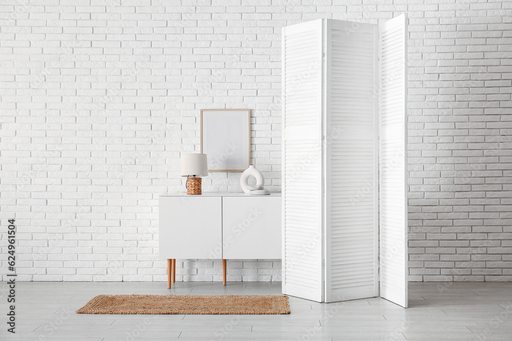 Folding screen with cabinet and lamp near white brick wall