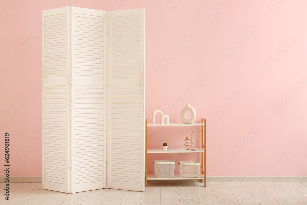 Folding screen and shelving unit near pink wall