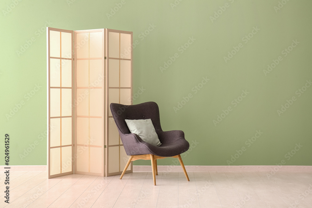 Folding screen and black armchair with pillow near green wall