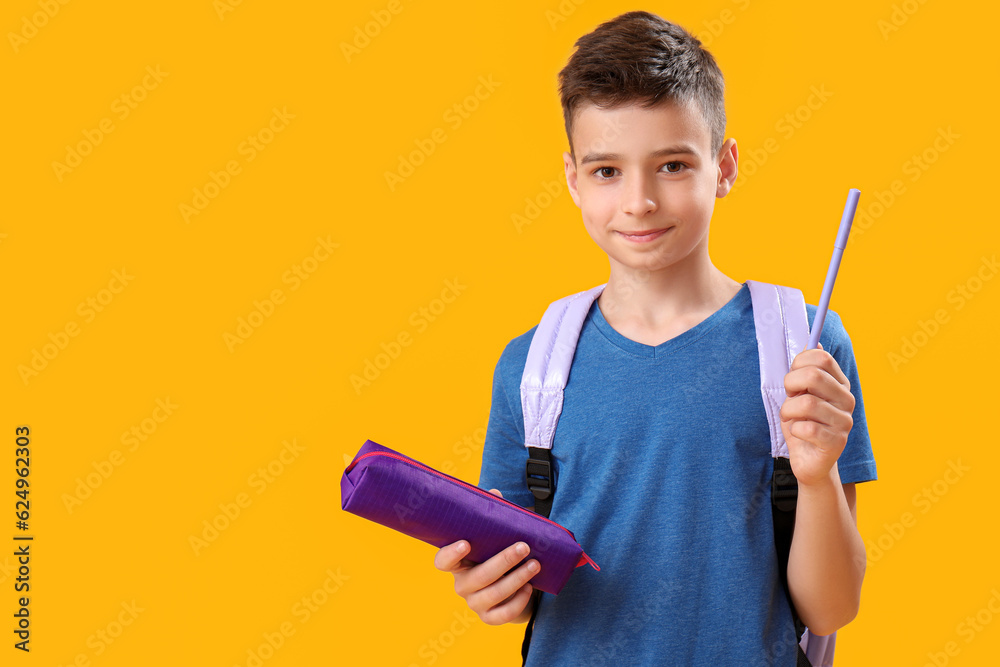 Little schoolboy with pencil case on orange background