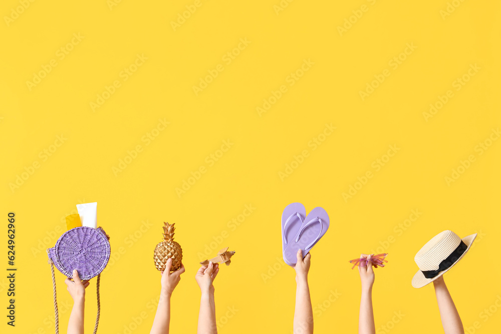 Many hands holding different beach accessories on yellow background