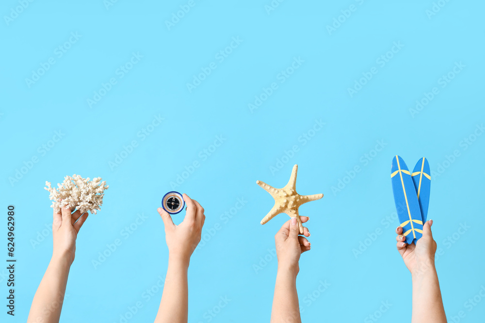 Female hands with coral, starfish, compass and mini surfboards on blue background