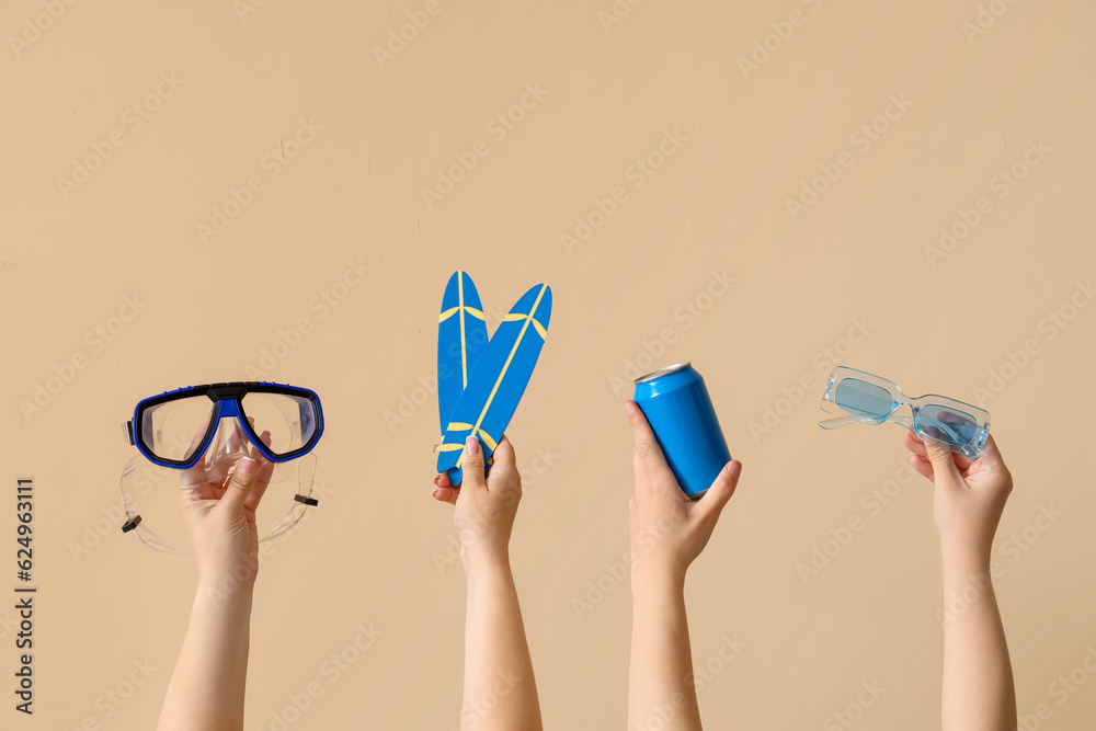 Female hands with beach accessories and can of soda on beige background