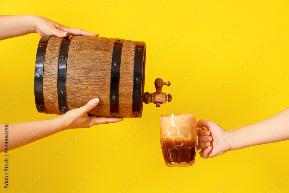 Woman pouring beer from barrel into mug on yellow background