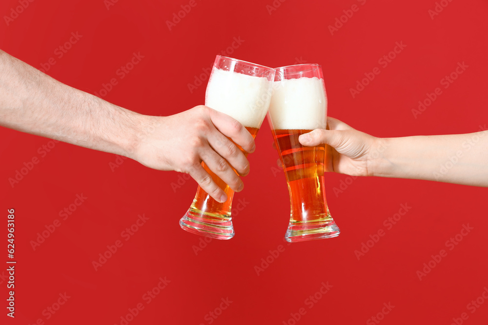 Man and woman with glasses of cold beer clinking on red background