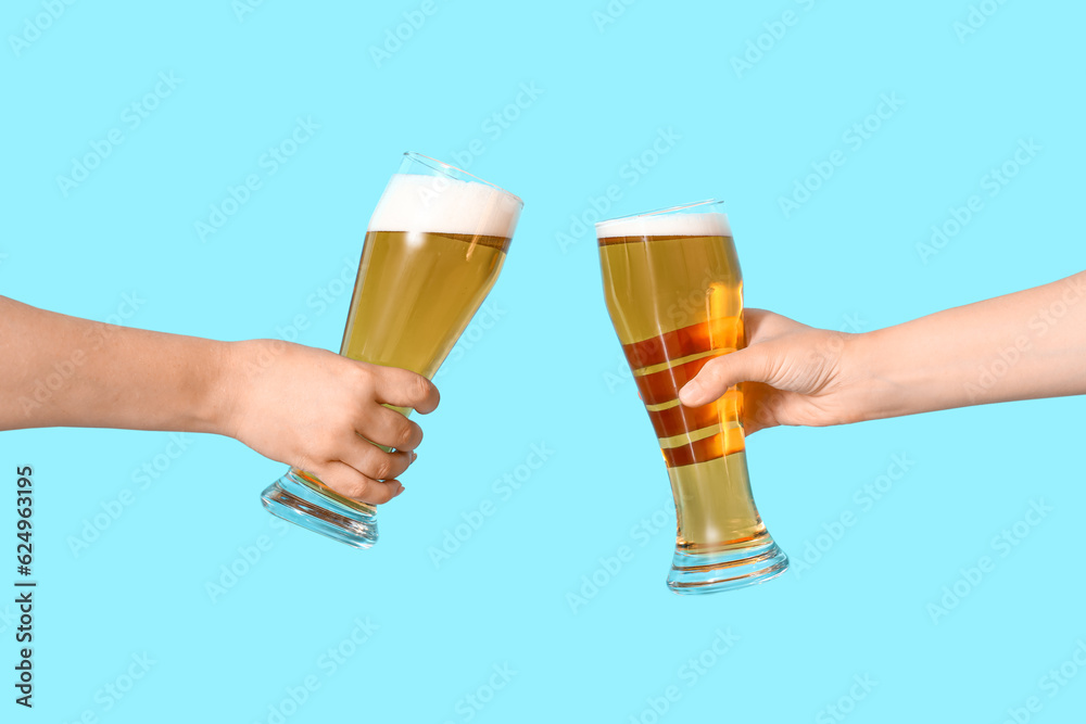 Female hands with glasses of cold beer clinking on blue background