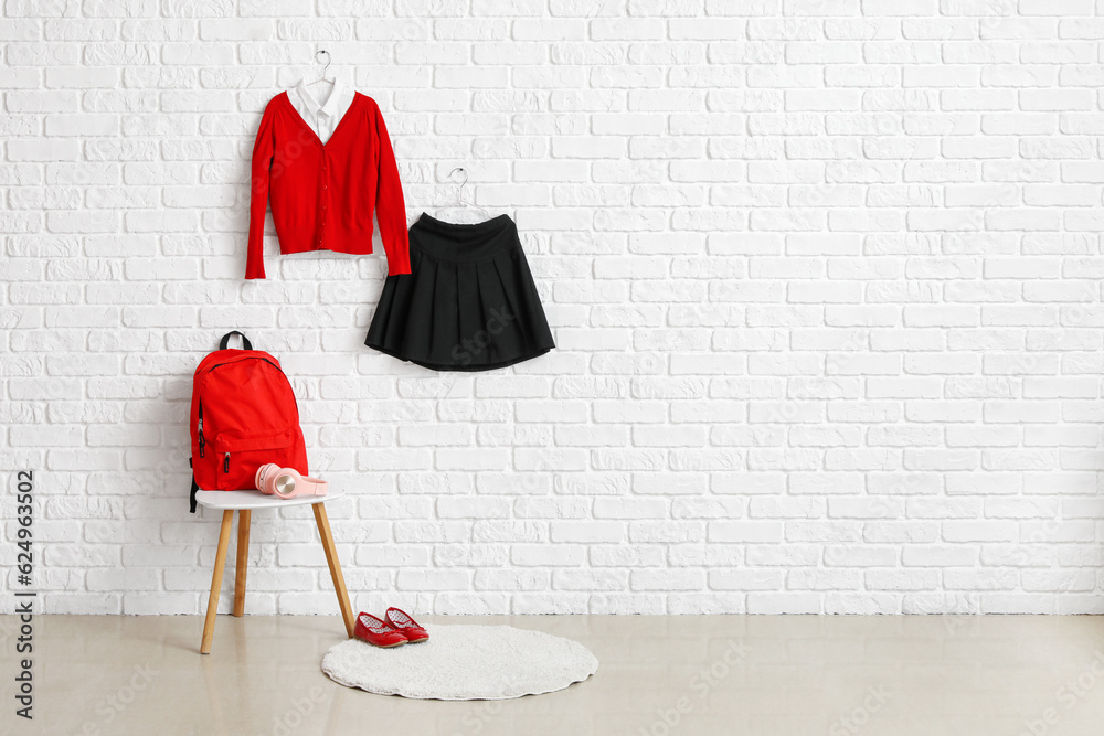 Table with backpack, shoes and stylish school uniform hanging on light brick wall in room