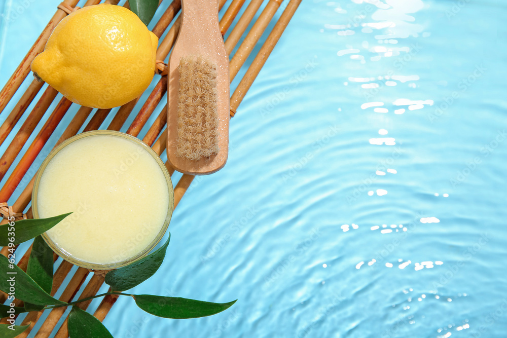 Bowl of lemon body scrub with massage brush on wooden stand in water