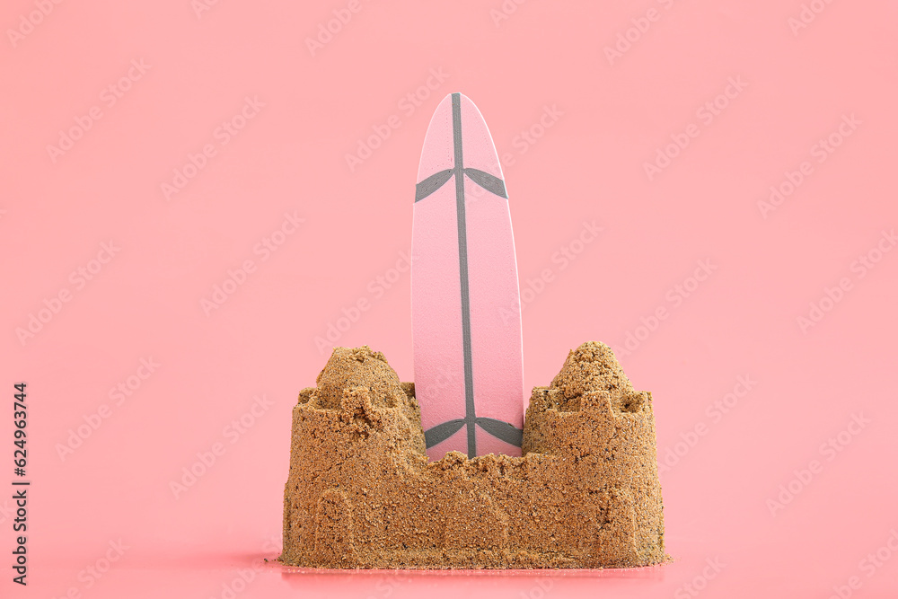 Castle made of sand with mini surfboard on pink background