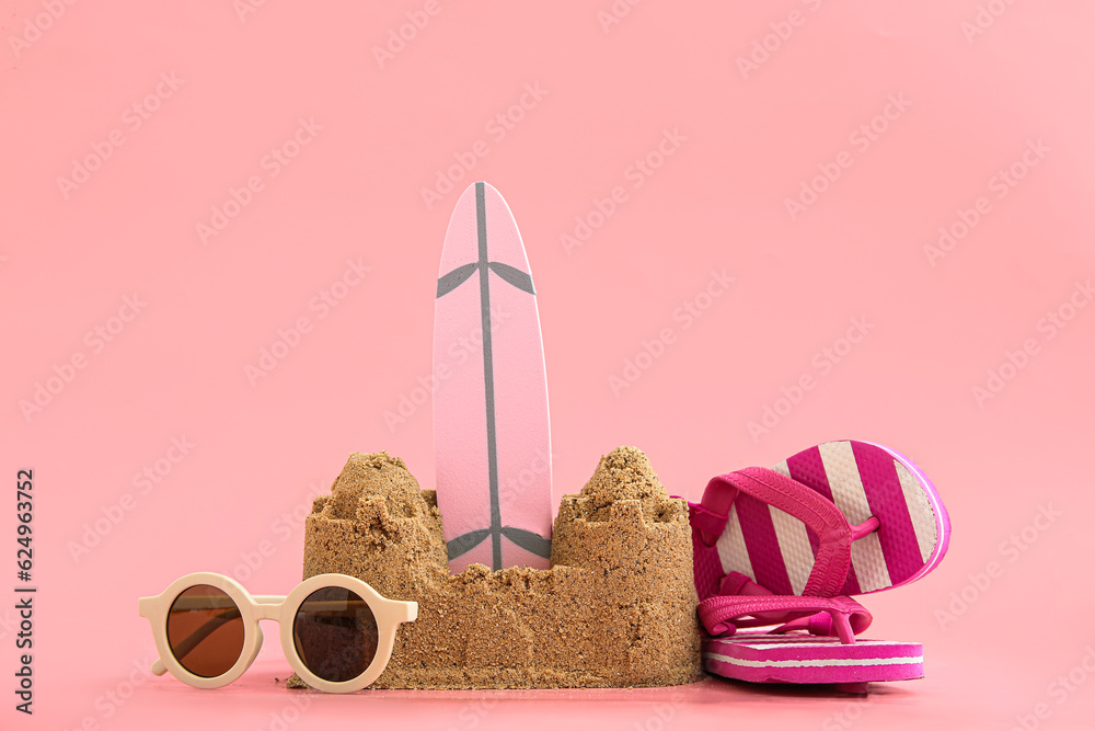 Castle made of sand with mini surfboard and beach accessories on pink background