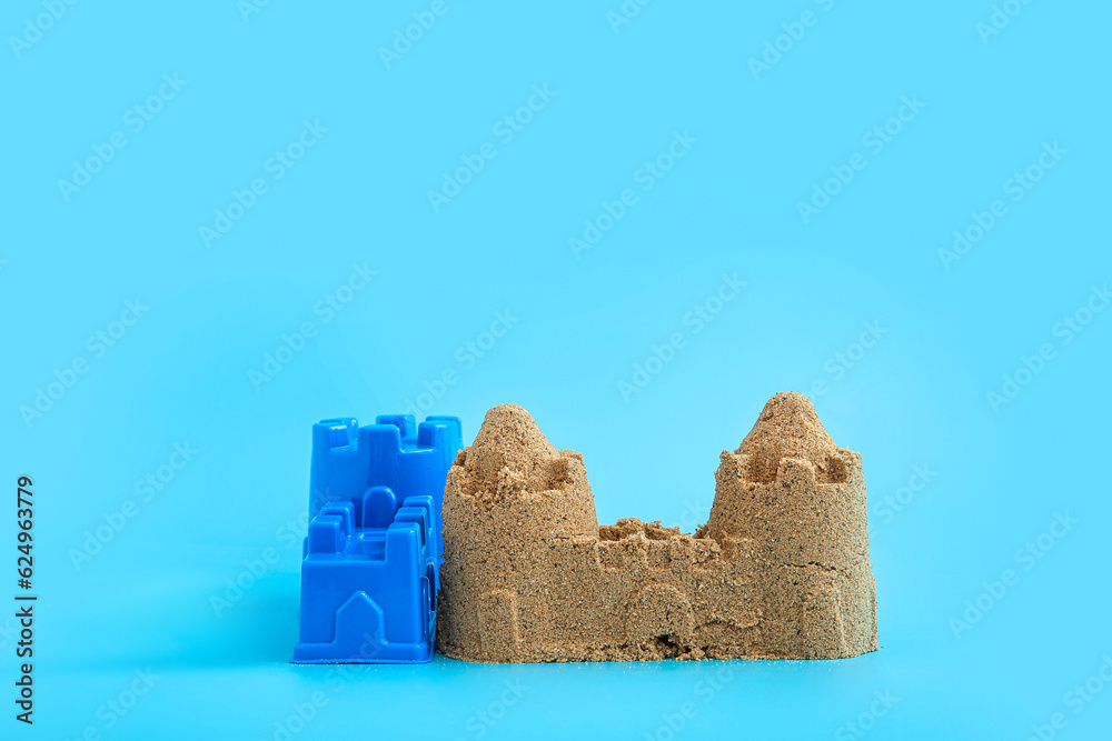 Castle made of sand with beach toy on blue background