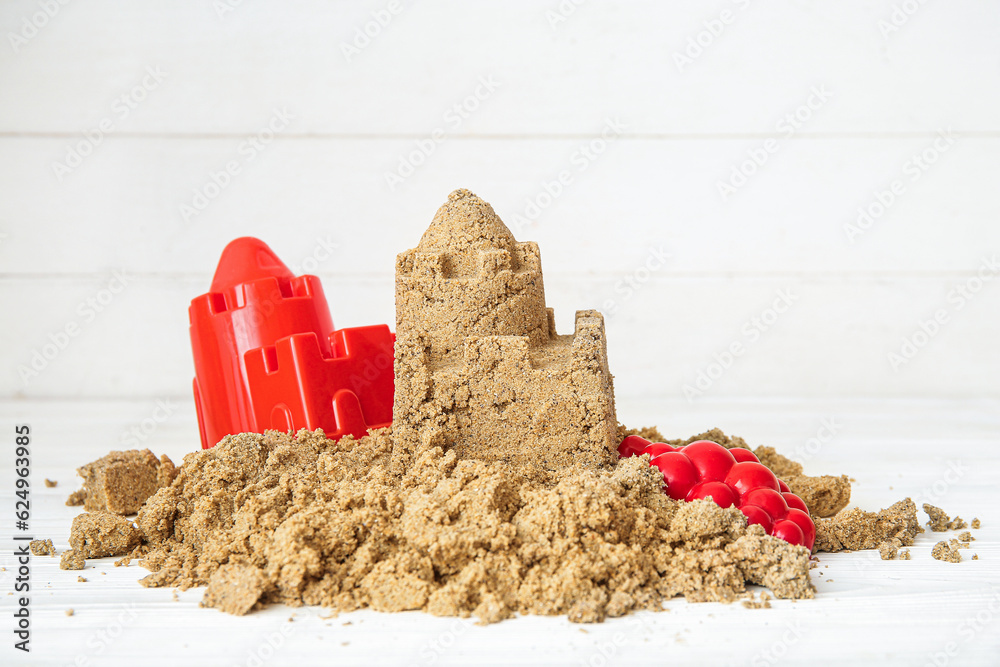 Castle made of sand with beach toys on white wooden background