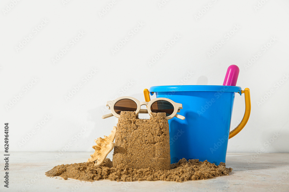 Castle made of sand with beach toys, starfish and sunglasses on white background