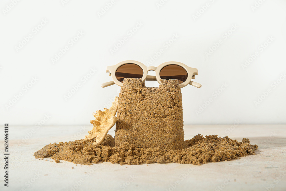 Castle made of sand with starfish and sunglasses on white background