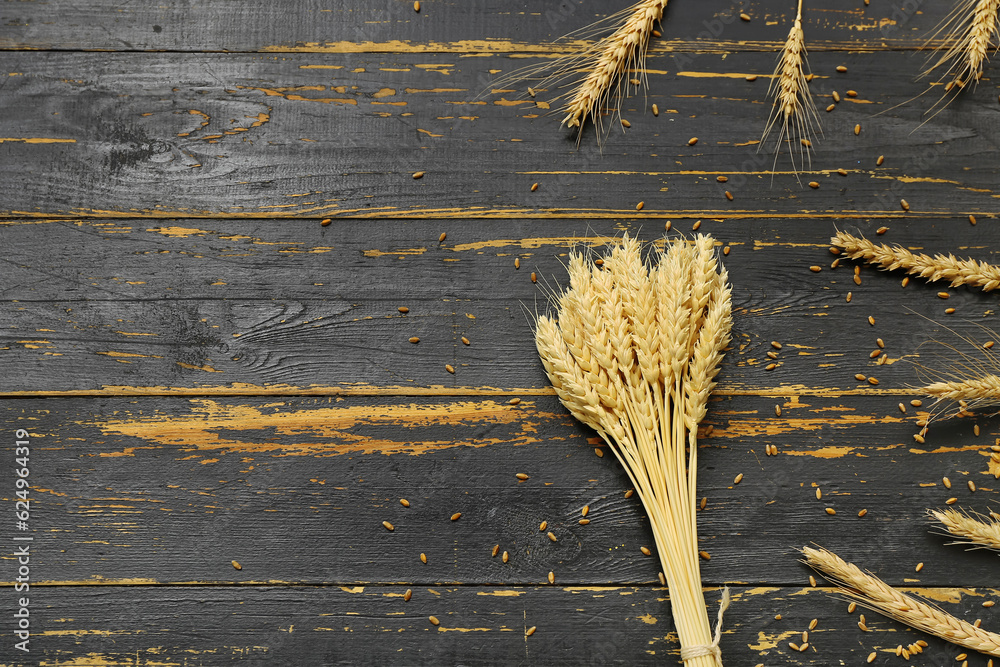 Bundle of wheat ears and grains on black wooden table