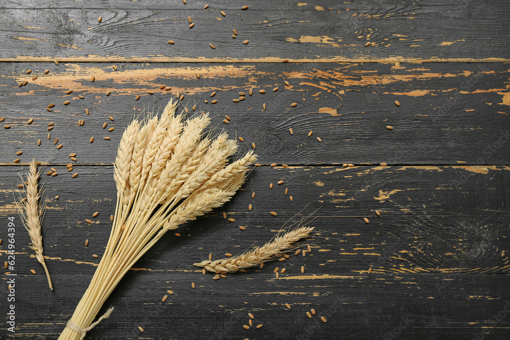 Bundle of wheat ears and grains on black wooden table