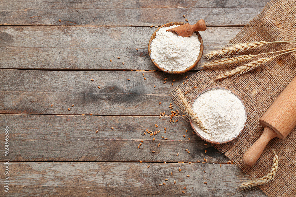 Bowls with wheat flour and rolling pin on wooden table