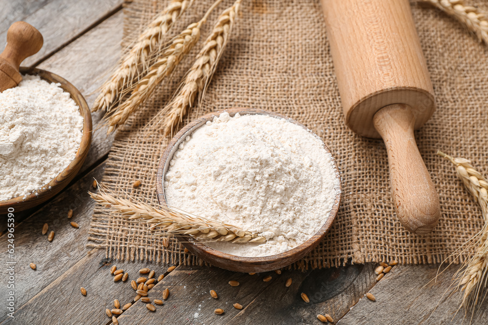 Bowls with wheat flour and rolling pin on wooden table