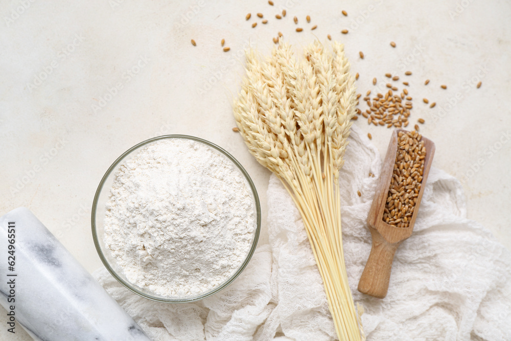 Wheat flour in glass bowl and spikelets on light background